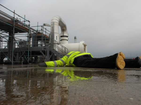 Injured person in a hi-viz jacket lying on the floor of an industrial site